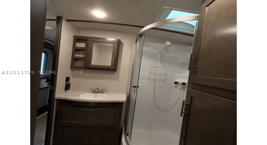 Bathroom featuring dark wood-finish cabinetry, a stone-pattern vanity countertop with an integrated basin, a curved glass-enclosed shower, a skylight, and wall-mounted medicine cabinet