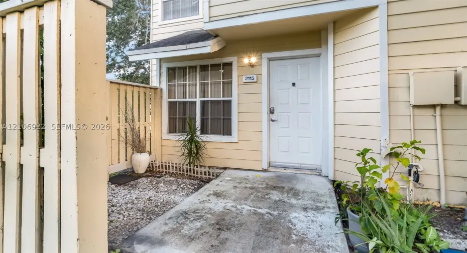 Exterior entry featuring light-toned horizontal siding, a private wood-style privacy fence, and a concrete patio