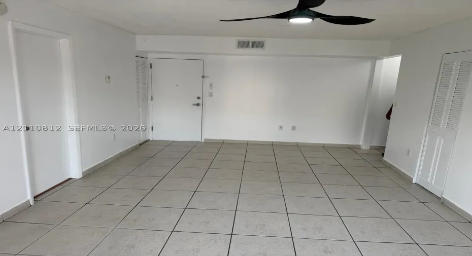 Neutral-toned tile flooring, three-blade ceiling fan with integrated light fixture, and multiple louvered-style closet doors