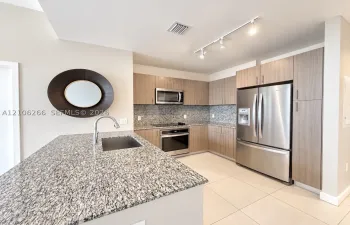 Kitchen featuring flat-panel wood-finish cabinetry, speckled stone countertops, stainless steel appliances, a center island with an undermount sink, and tile flooring