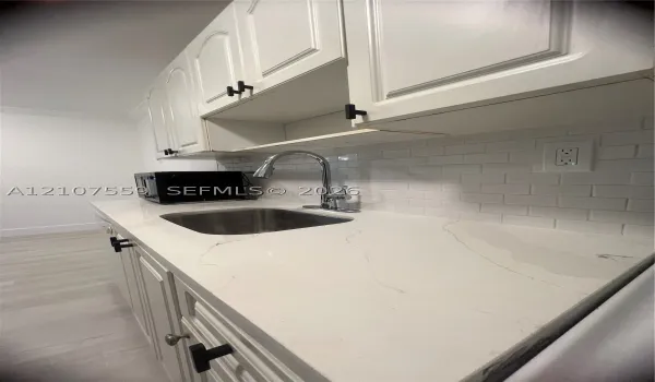 Kitchen featuring white cabinetry with matte black hardware, stone-finish countertops, stainless steel undermount sink with a gooseneck faucet, and white subway tile backsplash