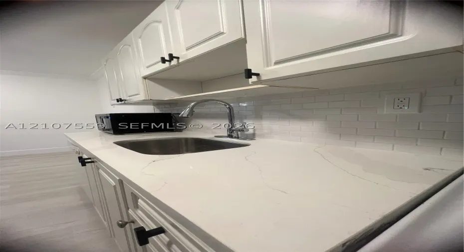 Kitchen featuring white cabinetry with matte black hardware, stone-finish countertops, stainless steel undermount sink with a gooseneck faucet, and white subway tile backsplash