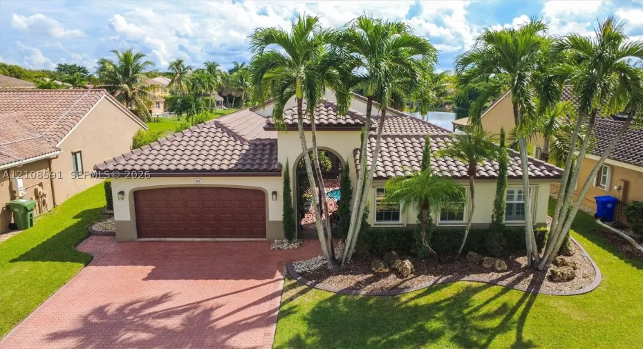 Single-story residence featuring a tile roof, arched entryway, two-car garage, brick-paver driveway, and mature landscaping