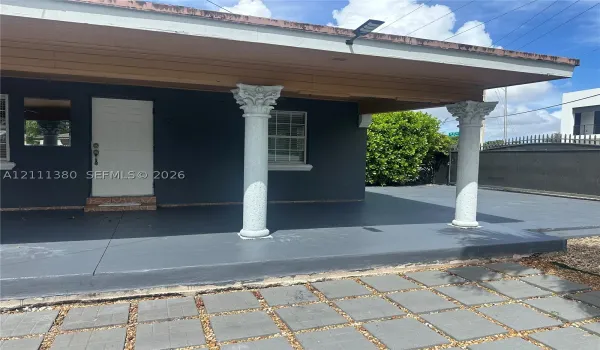 Covered front porch featuring decorative columns with ornate capitals, a paved hardscape entry, and a solid exterior door