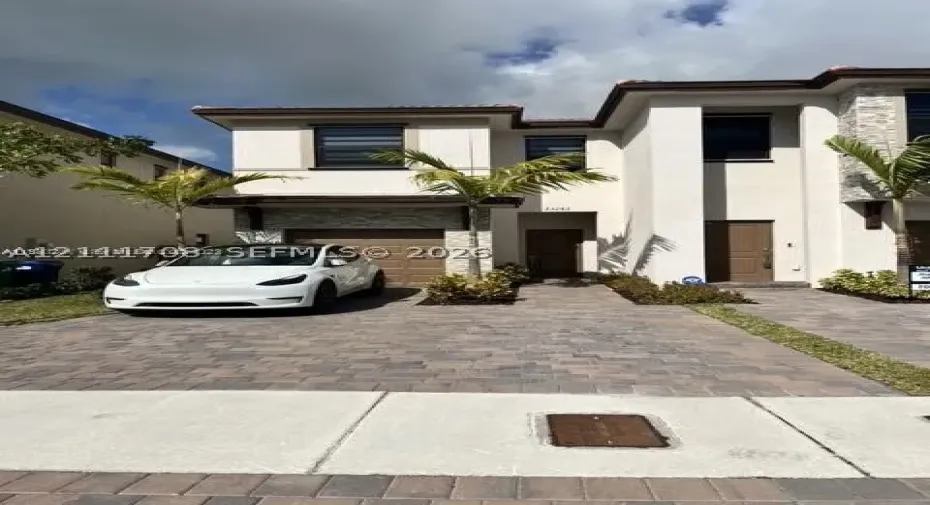 Two-story stucco exterior featuring stacked stone veneer accents, a paver driveway, an attached garage, and tiered landscaping