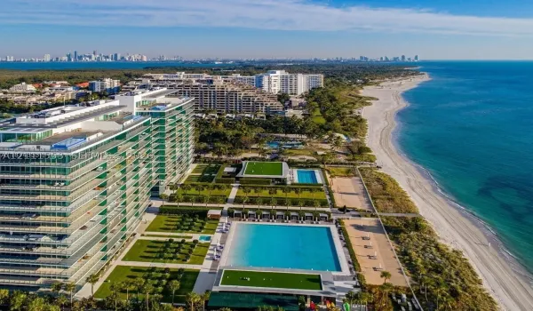 Direct oceanfront high-rise featuring expansive swimming pools, structured landscaping, manicured lawn areas, and sand beach access