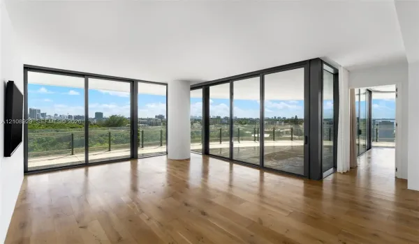 Floor-to-ceiling glass sliding doors, wood-finish flooring, and a wrap-around balcony with industrial-style metal railing