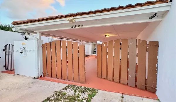 Covered carport featuring a terracotta-tiled roof, privacy-style wood fencing, and a supplemental metal gate entry
