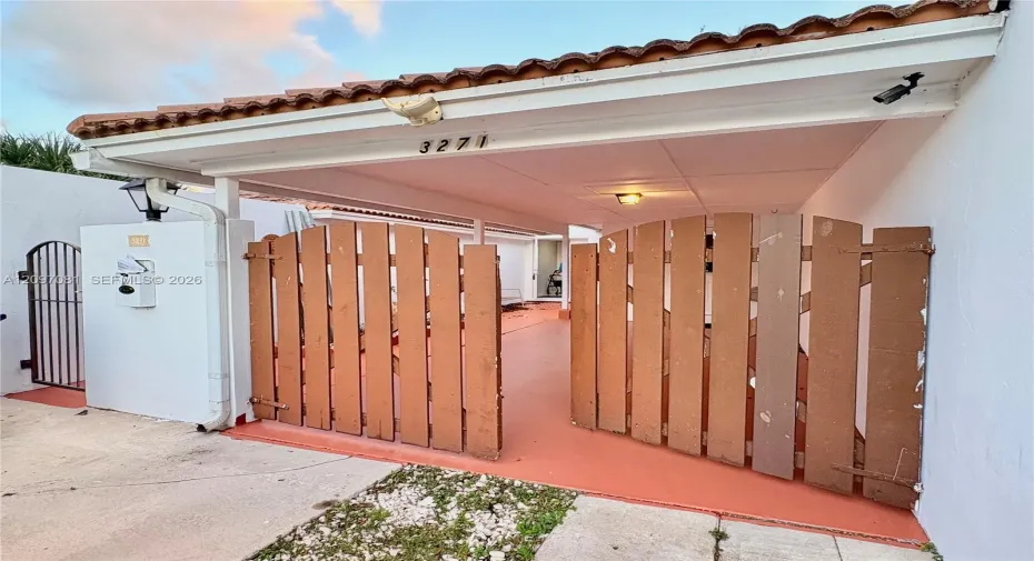 Covered carport featuring a terracotta-tiled roof, privacy-style wood fencing, and a supplemental metal gate entry