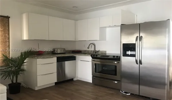Kitchen featuring white flat-panel cabinetry, stone countertops, stainless steel appliances, and wood-finish flooring