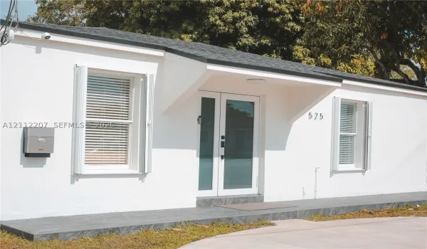 Exterior featuring smooth white stucco finish, dual-glass entry doors, dark stone-tile porch, and windows with white shutter accents