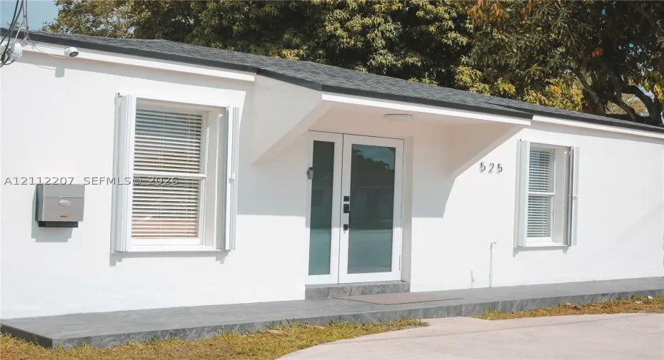 Exterior featuring smooth white stucco finish, dual-glass entry doors, dark stone-tile porch, and windows with white shutter accents