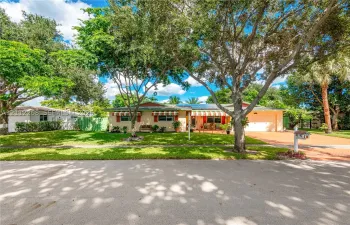 Single-story residence featuring a paved driveway, attached garage, solar panels, and mature landscaping