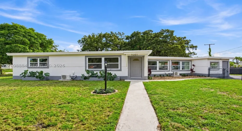 Single-story exterior featuring light-toned stucco siding, contrasting gray window trim, multiple horizontal windows, a central front entry door, and a concrete walkway