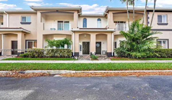 Two-story stucco exterior featuring arched architectural detailing, dual second-story covered balconies with white metal railings, and stone-paved entryway paths