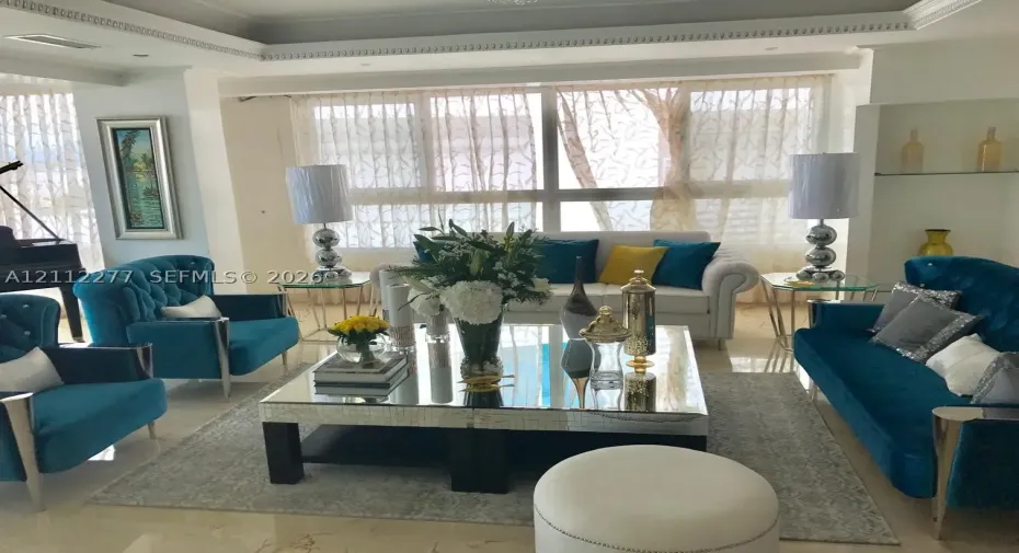 Living area featuring large-format polished stone flooring, crown molding, floor-to-ceiling windows with integrated window treatments, and built-in recessed shelving