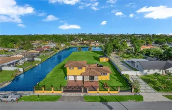 Waterfront residential property featuring expansive lawn space, decorative perimeter fencing, concrete driveway, and attached garage