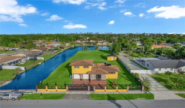 Waterfront residential property featuring expansive lawn space, decorative perimeter fencing, concrete driveway, and attached garage