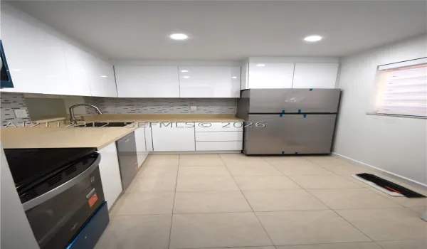 Kitchen featuring high-gloss white cabinetry, solid-surface countertops, a mosaic tile backsplash, stainless steel appliances, and large-format tile flooring