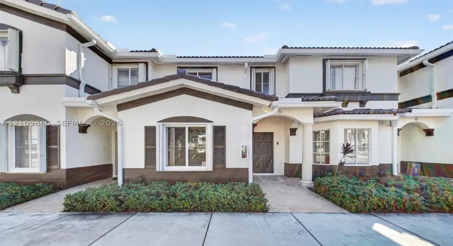 Two-story exterior featuring a light-toned stucco finish with contrasting dark trim, a covered entryway with a decorative pillar, and low-profile landscaping