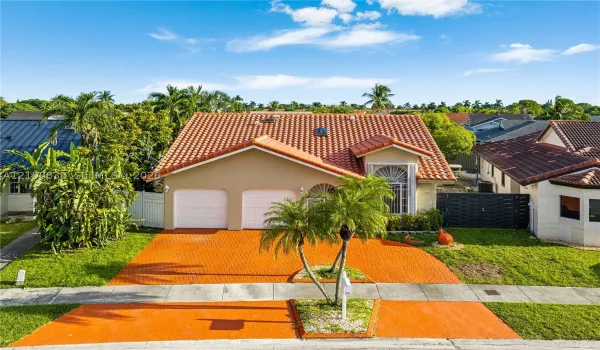 Single-story residence featuring a clay tile roof, dual-bay garage with paneled doors, arched window detailing, and an expansive paved driveway