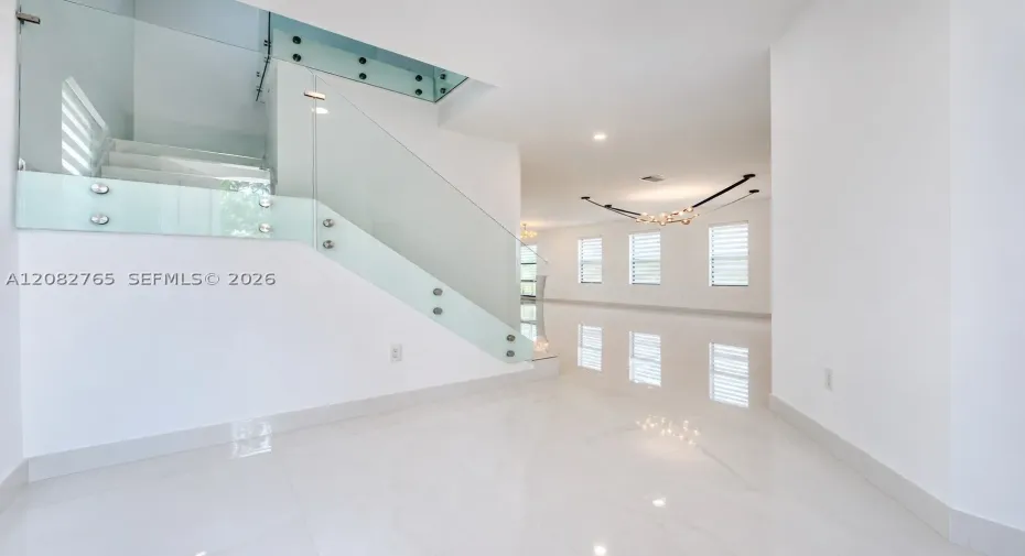 Staircase featuring a frameless glass railing with metal standoffs, large-format tile flooring, multiple double-hung windows, and a sculptural multi-light fixture