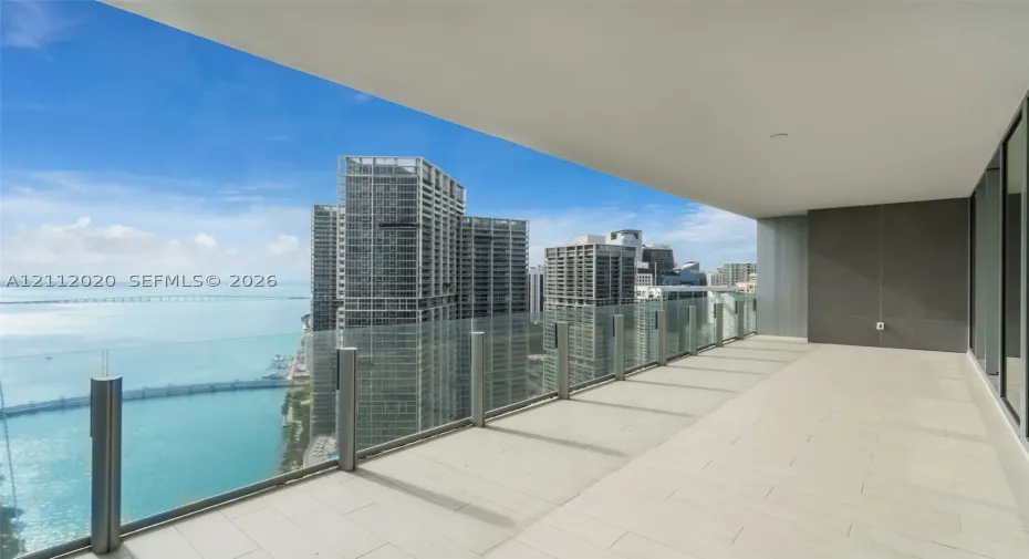 Expansive covered balcony featuring large-format tile flooring, a frameless glass railing, and structural concrete ceiling