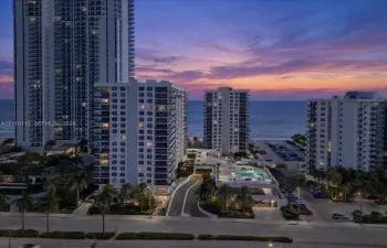 High-rise coastal residential structures featuring private balconies, an elevated swimming pool, and mature palm landscaping with a direct oceanfront backdrop