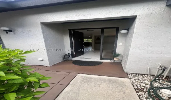 Covered entryway featuring a textured stucco facade, integrated globe lighting, and a front door with a matching side light panel