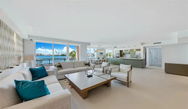 Open-concept living area featuring large-format tile flooring, floor-to-ceiling glass sliding doors, textured accent wall paneling, and an island kitchen with quartz countertops