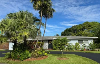 Single-story exterior featuring light-toned horizontal siding, a stone veneer facade, an asphalt driveway, and mature palm trees