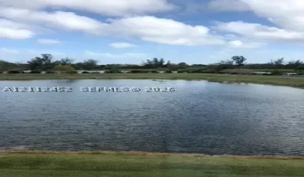Natural pond featuring a perimeter of mature trees and expansive grass lawn