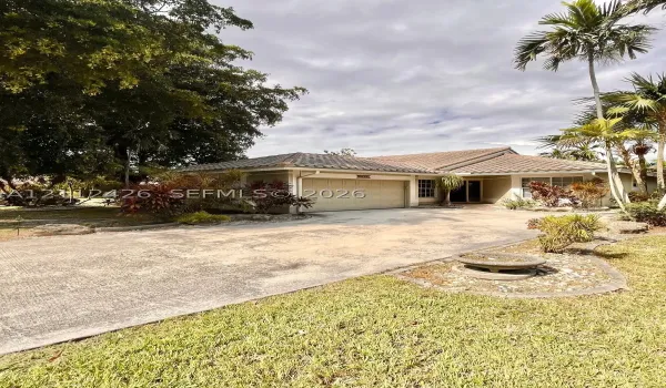 Single-story residence featuring a tile roof, an attached two-car garage, an expansive concrete driveway, and established palm and tropical landscaping