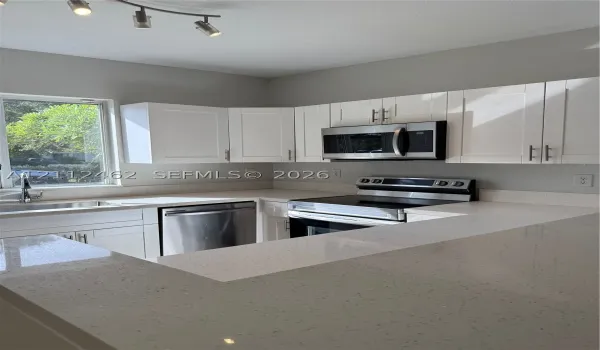 Kitchen featuring white shaker-style cabinetry, quartz countertops, stainless steel appliances, and a single-basin undermount sink