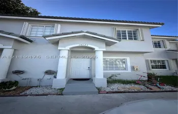 Two-story stucco exterior featuring a covered entryway with structural columns, multi-pane windows, and a dedicated concrete pathway