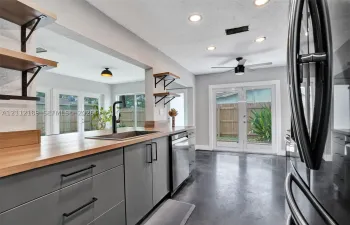 Kitchen featuring matte gray cabinetry, butcher block countertops, open wall-mounted shelving, polished concrete flooring, and stainless steel dishwasher