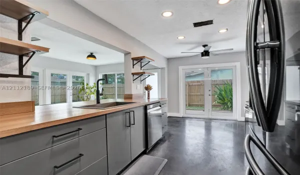 Kitchen featuring matte gray cabinetry, butcher block countertops, open wall-mounted shelving, polished concrete flooring, and stainless steel dishwasher