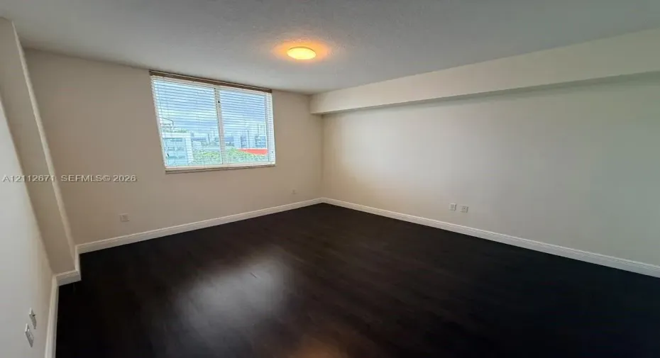 Room featuring dark wood-finish flooring, neutral wall tones, and a large window with horizontal blinds