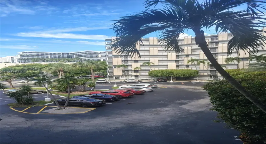Multi-story building featuring concrete balconies, landscaped grounds with palm trees, and paved surface parking
