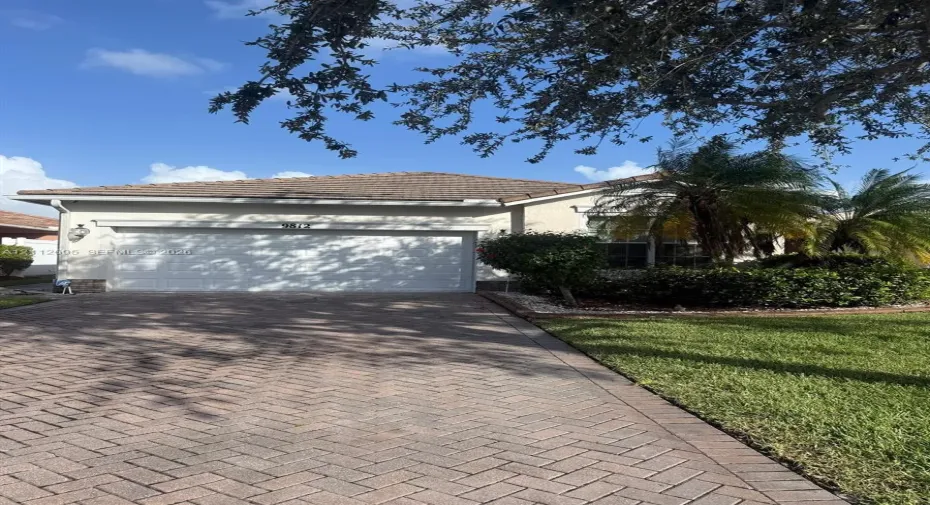 Stucco exterior featuring a tiled hip roof, two-car garage, herringbone-patterned paver driveway, and manicured landscaping