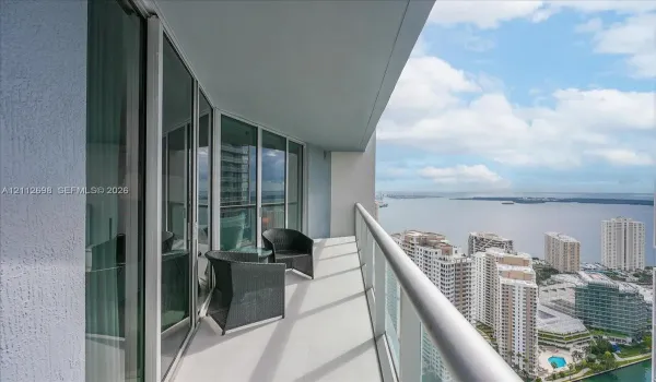Covered balcony featuring floor-to-ceiling glass doors, a metal railing, and high-rise water and cityscape orientation