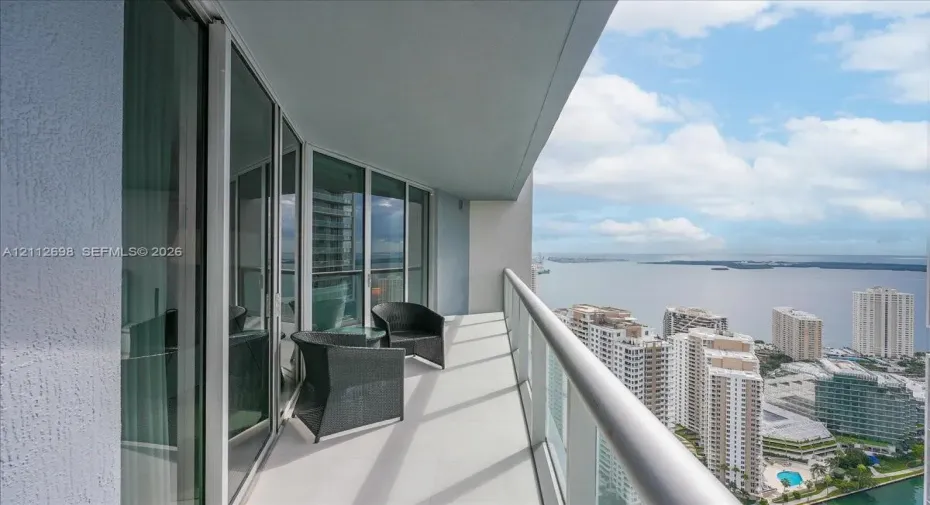 Covered balcony featuring floor-to-ceiling glass doors, a metal railing, and high-rise water and cityscape orientation