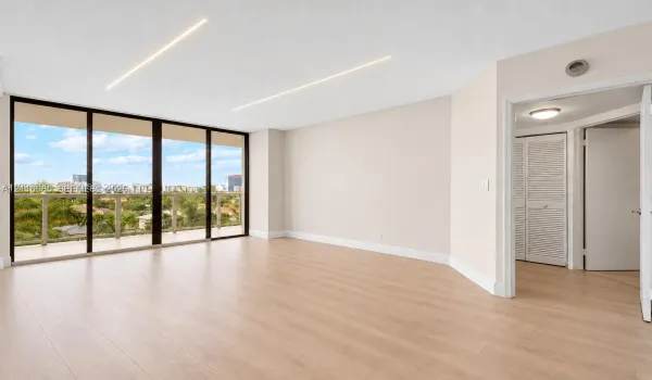 Virtually edited photo (digitally emptied/staged). Open-concept living space featuring floor-to-ceiling glass panel doors, wood-finish flooring, recessed linear lighting, and a closet with louvered doors.