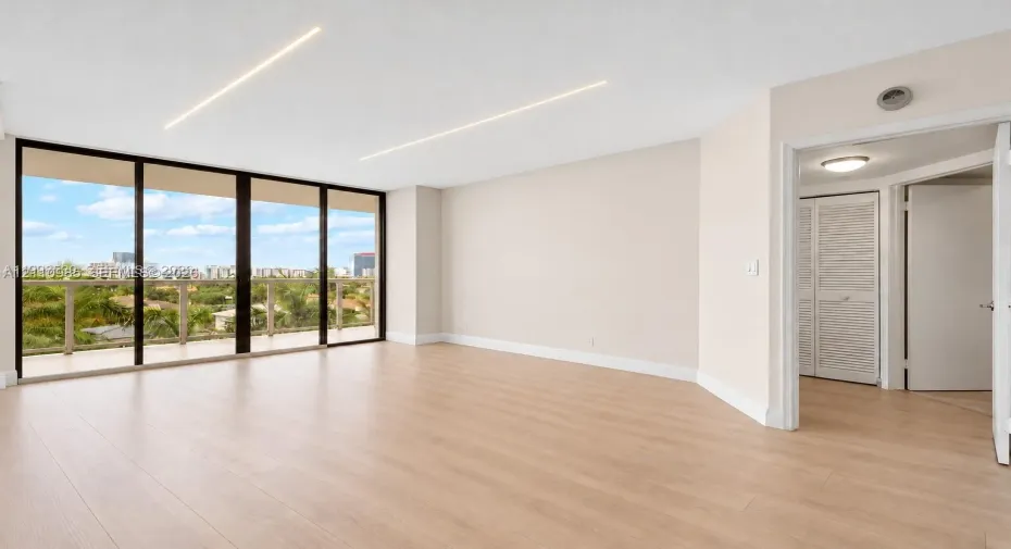 Virtually edited photo (digitally emptied/staged). Open-concept living space featuring floor-to-ceiling glass panel doors, wood-finish flooring, recessed linear lighting, and a closet with louvered doors.