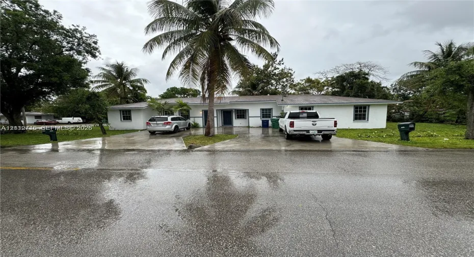 Single-story residence featuring a white exterior, hip roof, dual paved driveways, and mature palm trees