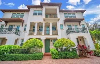 Stucco multi-story exterior featuring a tile roof, multiple wrought-iron balconies, arched entryway detailing, and brick-paver hardscaping