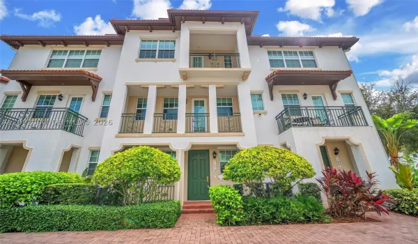 Stucco multi-story exterior featuring a tile roof, multiple wrought-iron balconies, arched entryway detailing, and brick-paver hardscaping