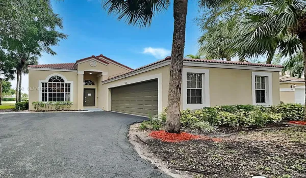 Stucco exterior residence featuring a multi-car garage, tile roofing, arched window detailing, and manicured landscaping