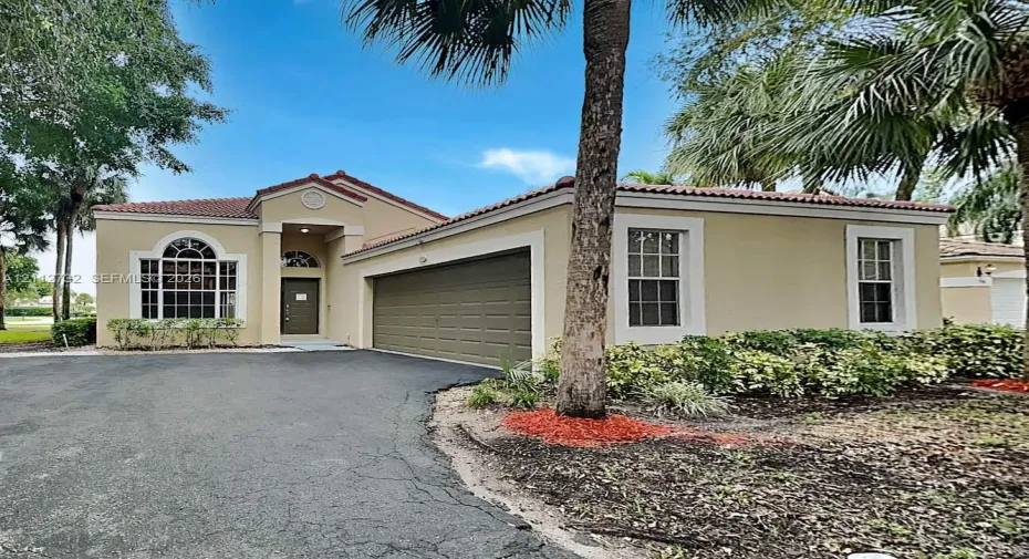Stucco exterior residence featuring a multi-car garage, tile roofing, arched window detailing, and manicured landscaping