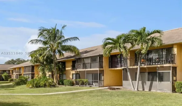 Stucco exterior featuring screened-in lanais, private balconies with metal railings, and mature palm trees situated on landscaped grounds